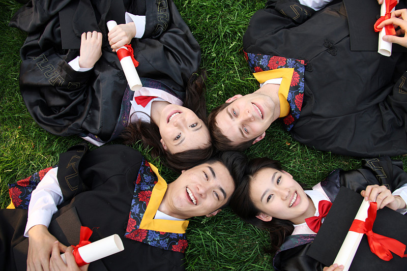 四个身穿学士服的大学生躺在草地上图片素材