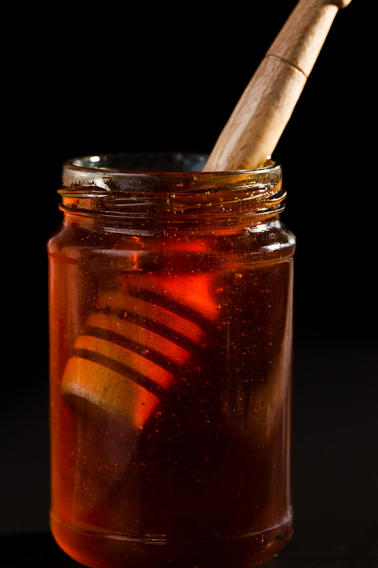 蜂蜜勺在一个蜂蜜罐子在一个黑色的背景图片素材