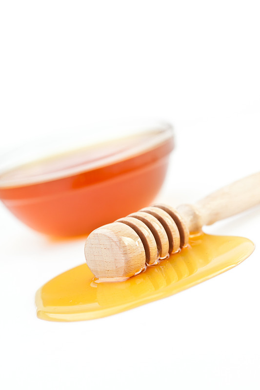 在白色的背景下，蜂蜜勺在蜂蜜碗前洒出蜂蜜图片下载