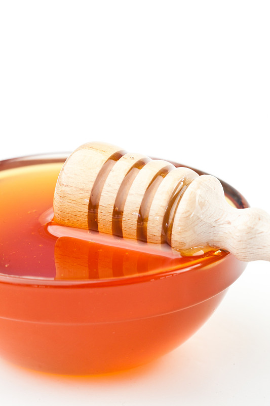 蜂蜜勺横向放在碗的边缘，以白色为背景图片下载