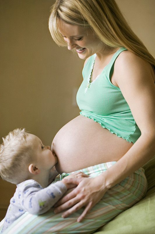 儿子(4-5)坐在床上亲吻孕妇的肚子图片下载