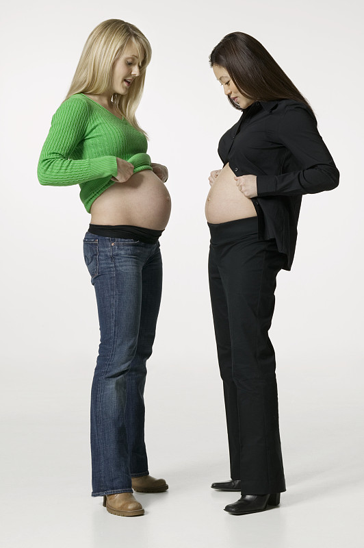 两个孕妇比较腹部在工作室，肖像图片下载