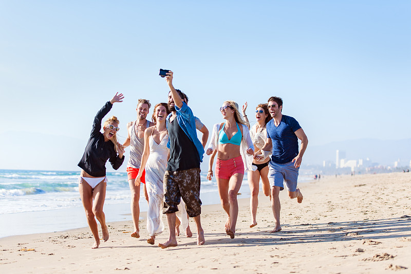 一群朋友在海滩上跑步和拍摄图片素材