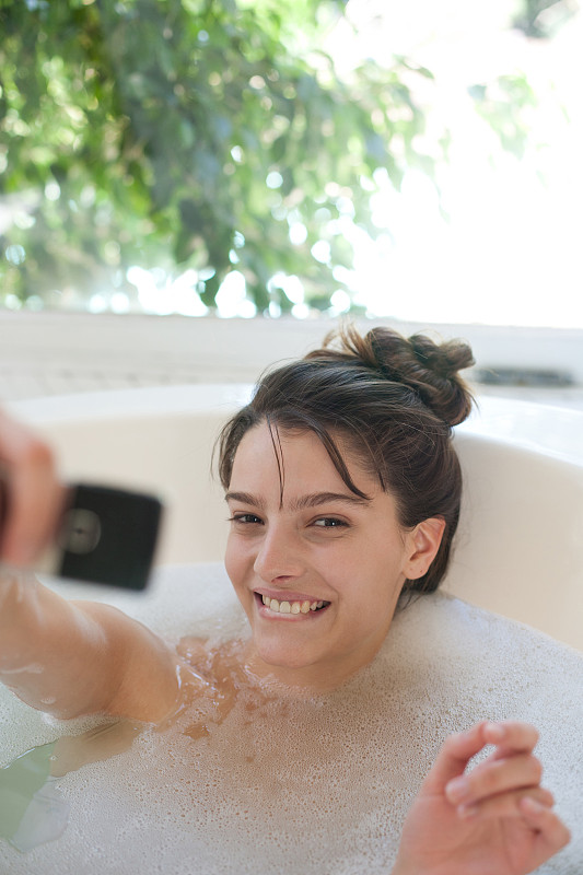 女人放松在泡泡浴中使用手机和微笑图片下载
