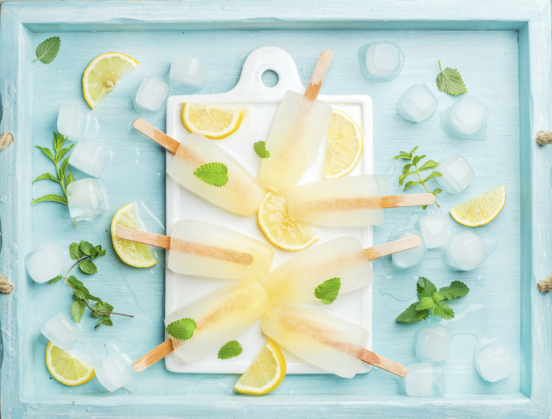 白色的陶瓷板上放着柠檬冰棒，配上柠檬片、冰块和薄荷叶，以蓝绿色为背景图片下载