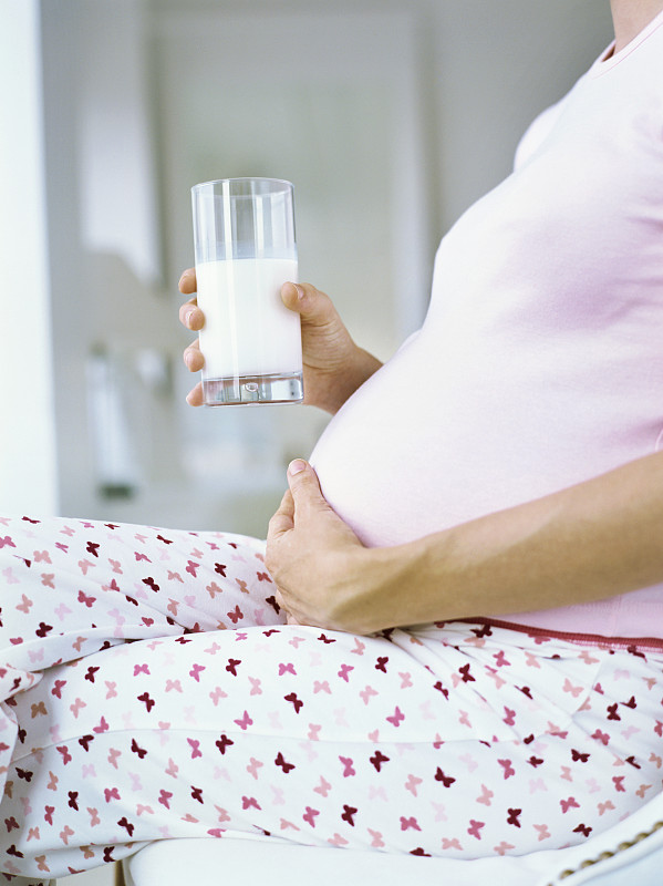 中段视图的孕妇持有一杯牛奶和触摸她的腹部图片下载