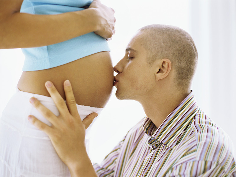 一个年轻男子亲吻孕妇腹部的侧影图片下载
