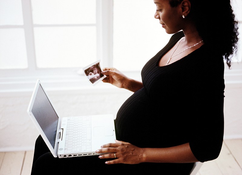 一个孕妇的侧影，她坐在电脑旁边，还有一张照片摄影图片下载