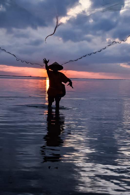 在日落时分，渔民在海面上撒渔网图片素材