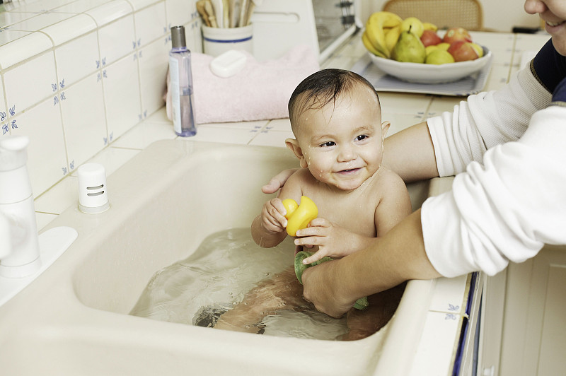父母在厨房水槽里给婴儿洗澡图片下载