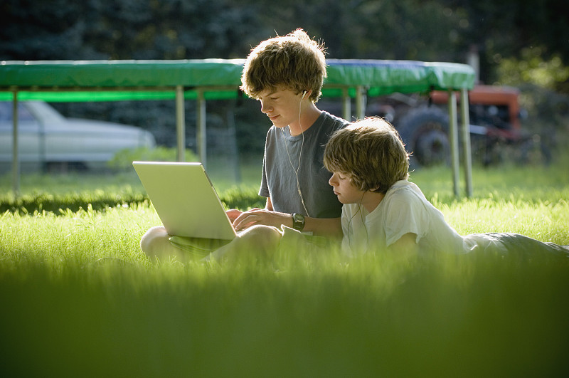男孩们坐在草地上用笔记本电脑图片下载