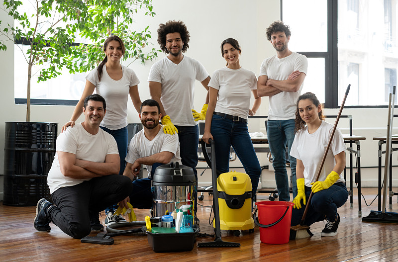 拉丁美洲多样化的清洁团队在一个办公室做一个微笑的镜头，同时拿着清洁设备图片下载
