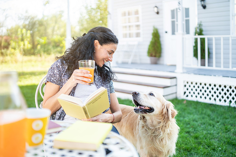微笑的中年妇女坐在她的金毛猎犬前院里读一本书图片下载