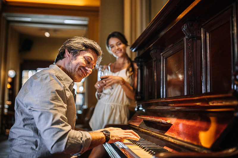 一个英俊的男人在餐馆为他的妻子弹钢琴图片下载