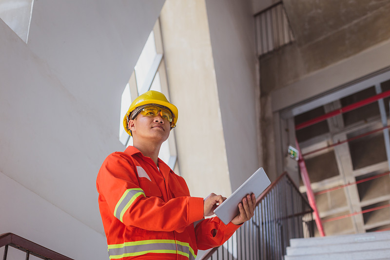 亚洲建筑或电子工程师戴安全帽穿安全夹克在建筑工地旁边用数码平板电脑，工程师在工地检查建筑项目图片素材