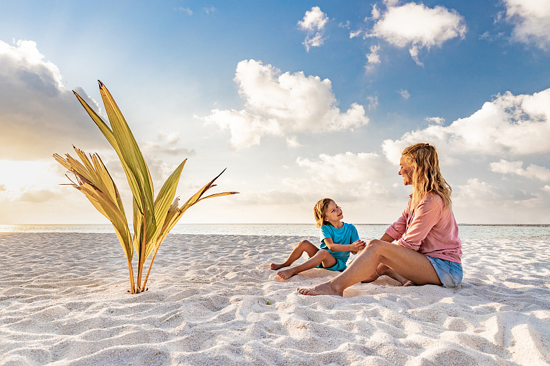 快乐的单身母亲在沙滩上和她的小男孩说话。图片素材
