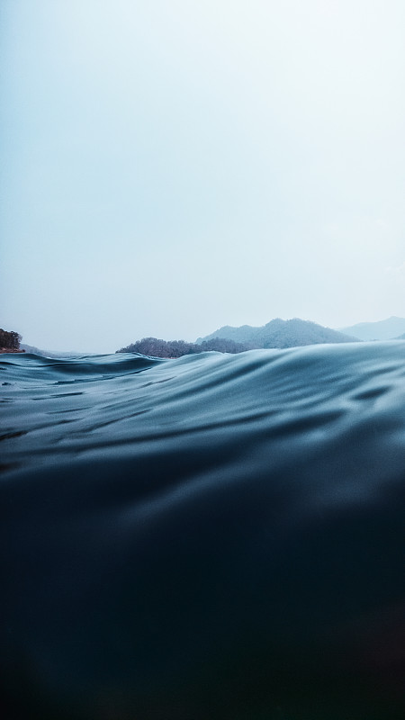 在湖岸边有山的深蓝色海水中，湖表面上下分开的一层图片素材
