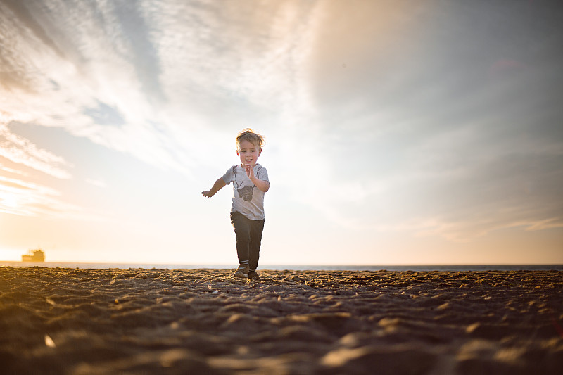 日落时分，男孩在海滩上朝着照相机跑去图片素材