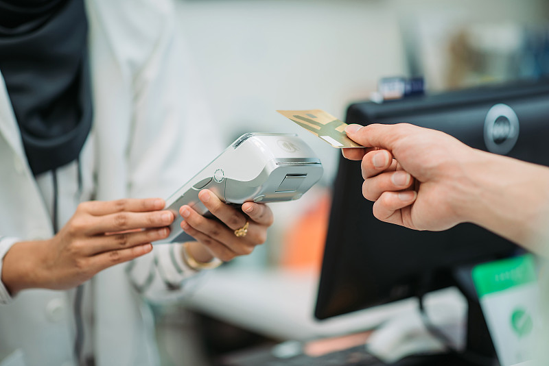 亚洲年轻的中国男性顾客微笑着在药店收银员用他的信用卡进行非接触式支付图片下载