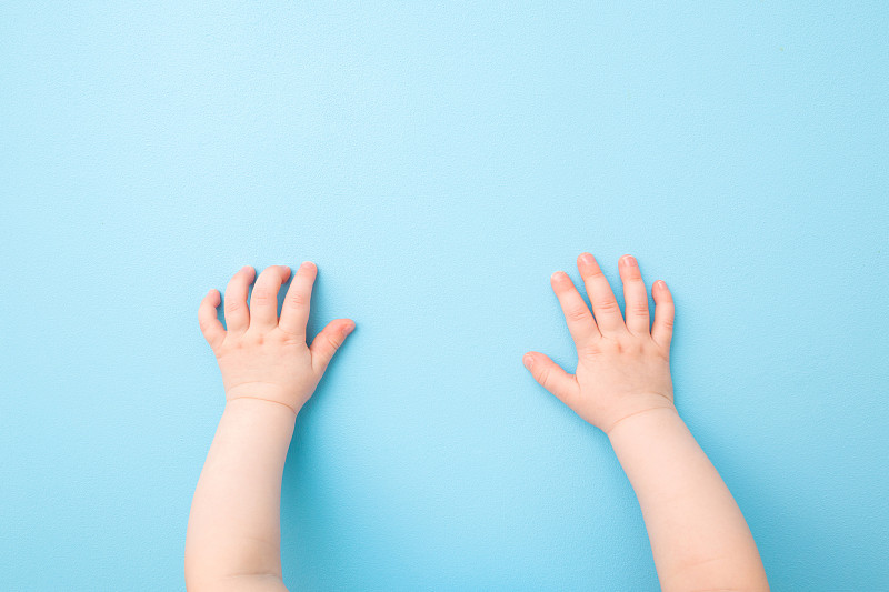 两只婴儿的手放在浅蓝色的桌子背景上。柔和的颜色。特写镜头。视角拍摄。自顶向下的观点。图片下载
