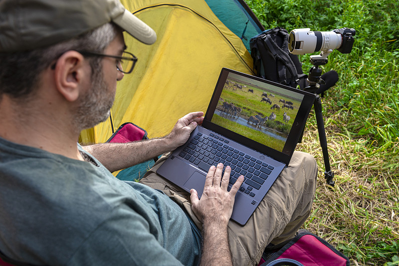 摄影师在帐篷里用笔记本电脑工作。图片素材