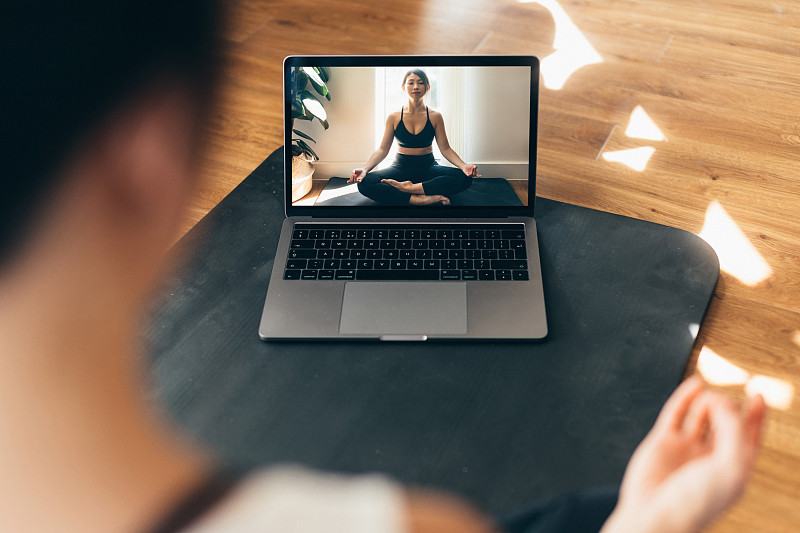 年轻女子练习瑜伽和冥想在笔记本电脑上的视频课。图片素材