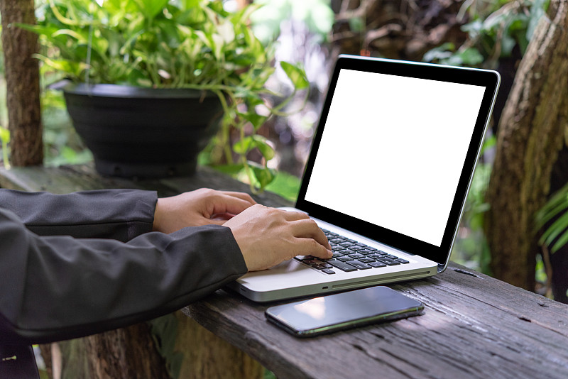 一位在户外花园使用笔记本电脑的亚洲女性。图片下载