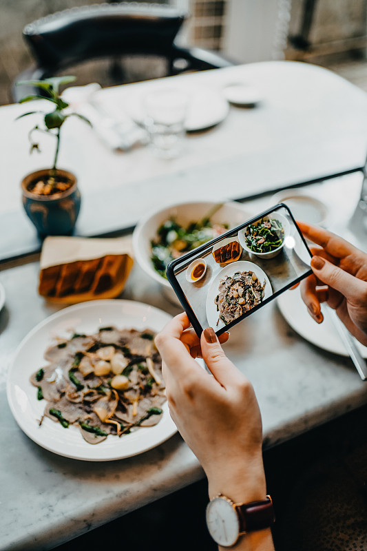 在一家餐馆里，一位女士在用智能手机进食前，用手拍下了刚上桌的食物图片素材