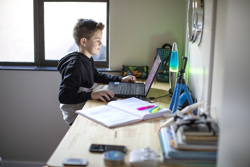 一个九岁的男孩在家里用笔记本电脑做作业。图片素材