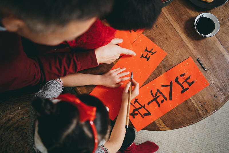 俯视图快乐的小孙女和孙子练习书法，为中国新年的对联与他们的祖父图片下载