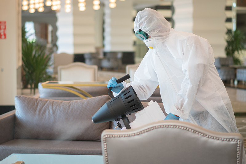 穿着防护服的人为酒店家具消毒。图片素材