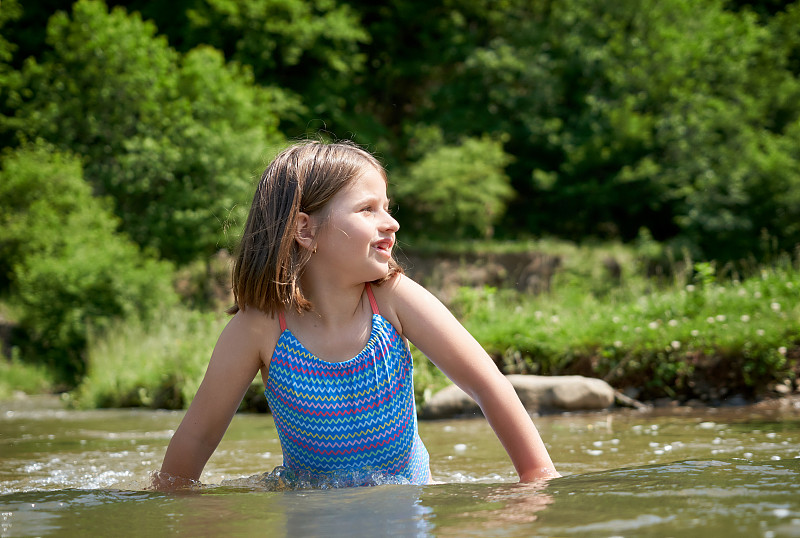 金发女孩尝试着山间河的冷水。图片素材