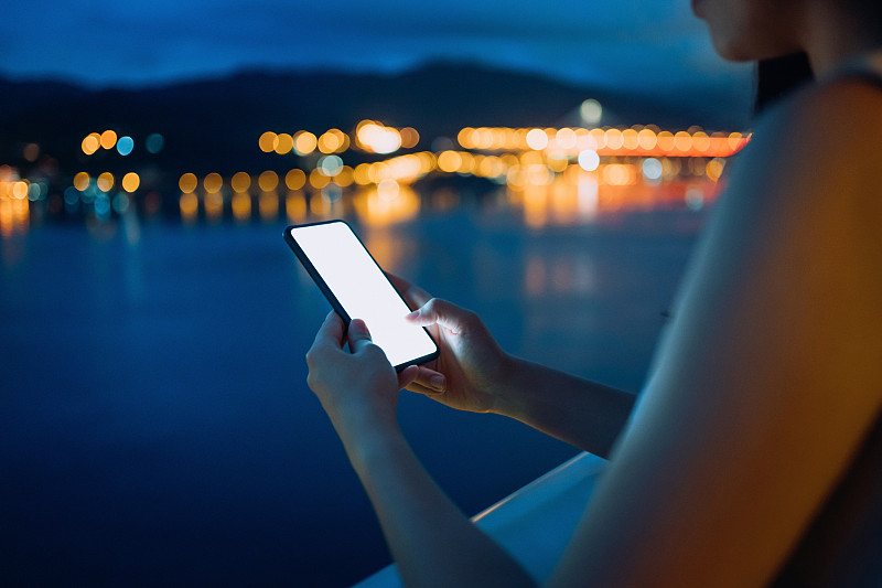 日落时分，年轻的亚洲女子在阳台上放松，在智能手机上玩社交媒体图片素材