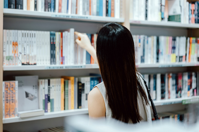 后视图的年轻亚洲妇女在书店的书架上寻找书籍图片素材