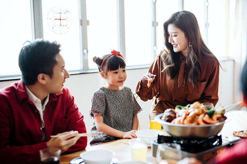 三代快乐的亚洲家庭庆祝春节，享用美味的传统中国菜团圆饭，母亲给女儿端菜图片素材