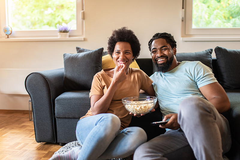 一对快乐的非裔美国夫妇在客厅看电影。图片下载