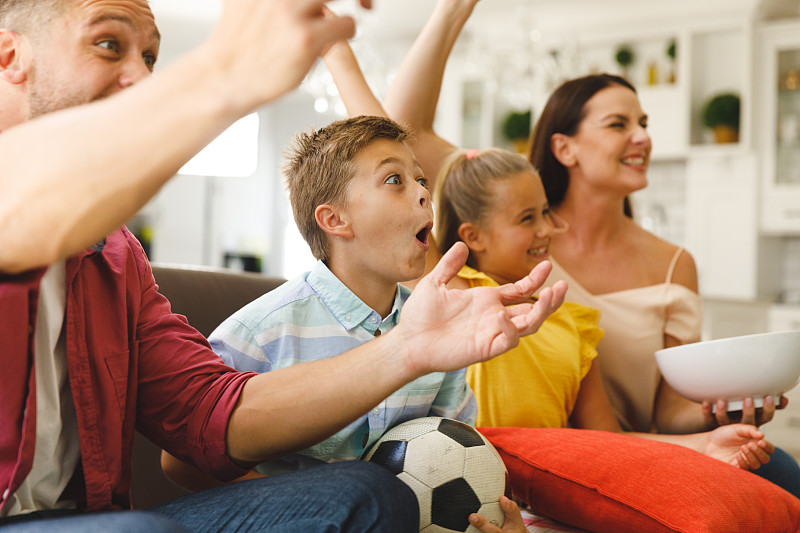 兴奋的白人父母坐在沙发上，女儿和儿子在看电视上的足球比赛并欢呼图片下载