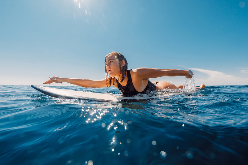 冲浪女孩在冲浪板上划船。迷人的冲浪女人在海洋和阳光的日子图片下载