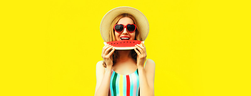 夏天的肖像快乐微笑的女人吃新鲜的西瓜片戴着草帽，红色的心形太阳镜在黄色的背景，空白的拷贝空间的广告文字图片下载