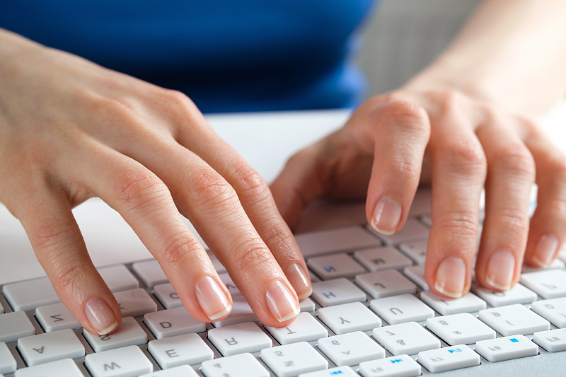 女性用手在电脑或笔记本电脑的键盘上打字。一个女人，坐在办公桌前的办公室职员。商业的概念，自由职业，在家工作。IT支持，网络安全，在线社会支持。网上远程学习。摄影图片