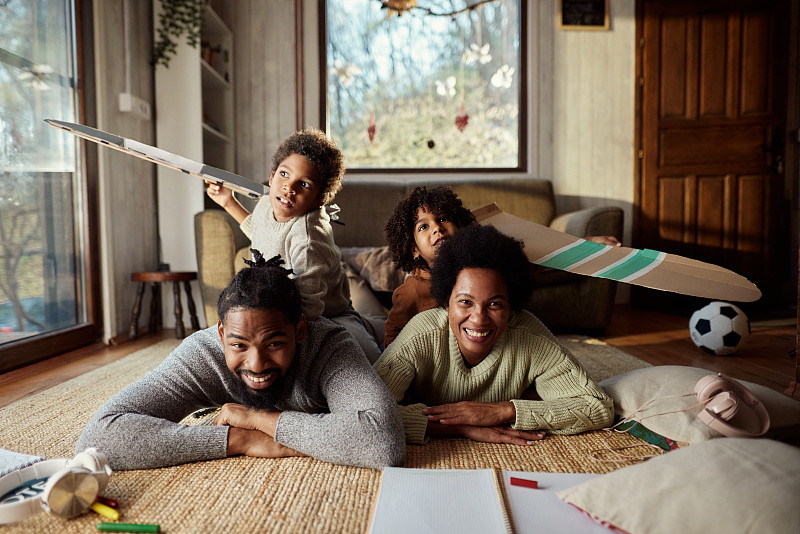 快乐的非裔美国家庭在家里的地毯上玩得很开心。图片下载