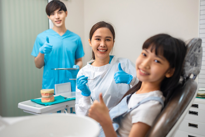 儿童牙科，牙齿健康。特写快乐的亚洲小女孩微笑着看着镜头，坐在牙医的椅子上，接受牙科治疗。图片下载