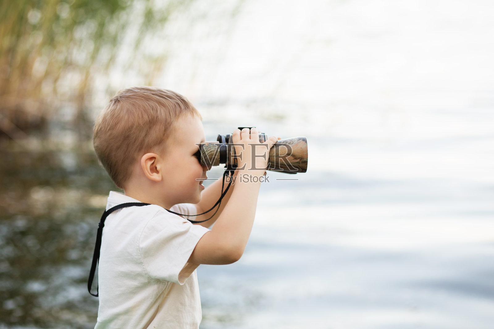 小男孩在河边用望远镜看照片摄影图片