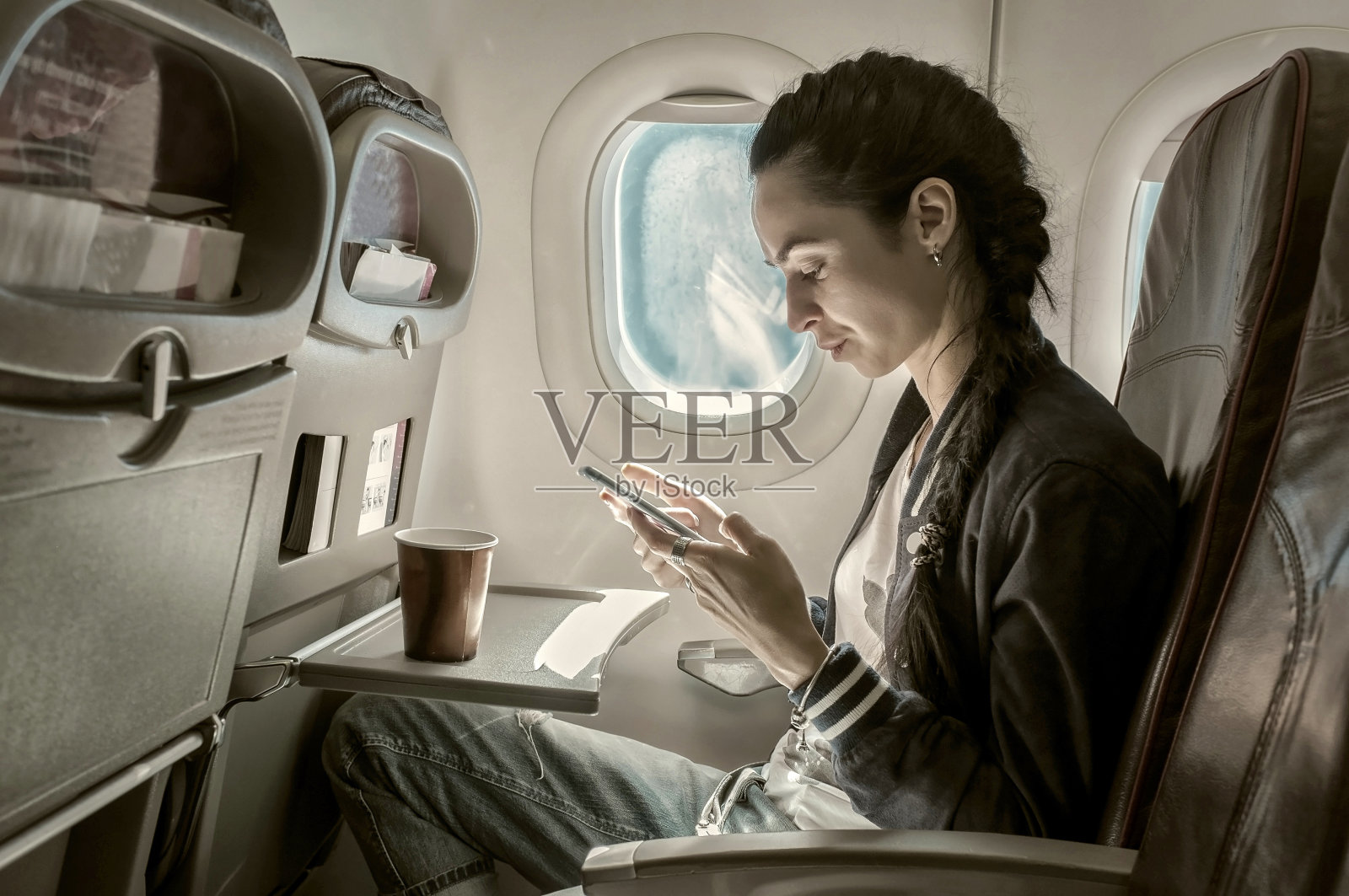 坐在飞机上看手机的女人。照片摄影图片
