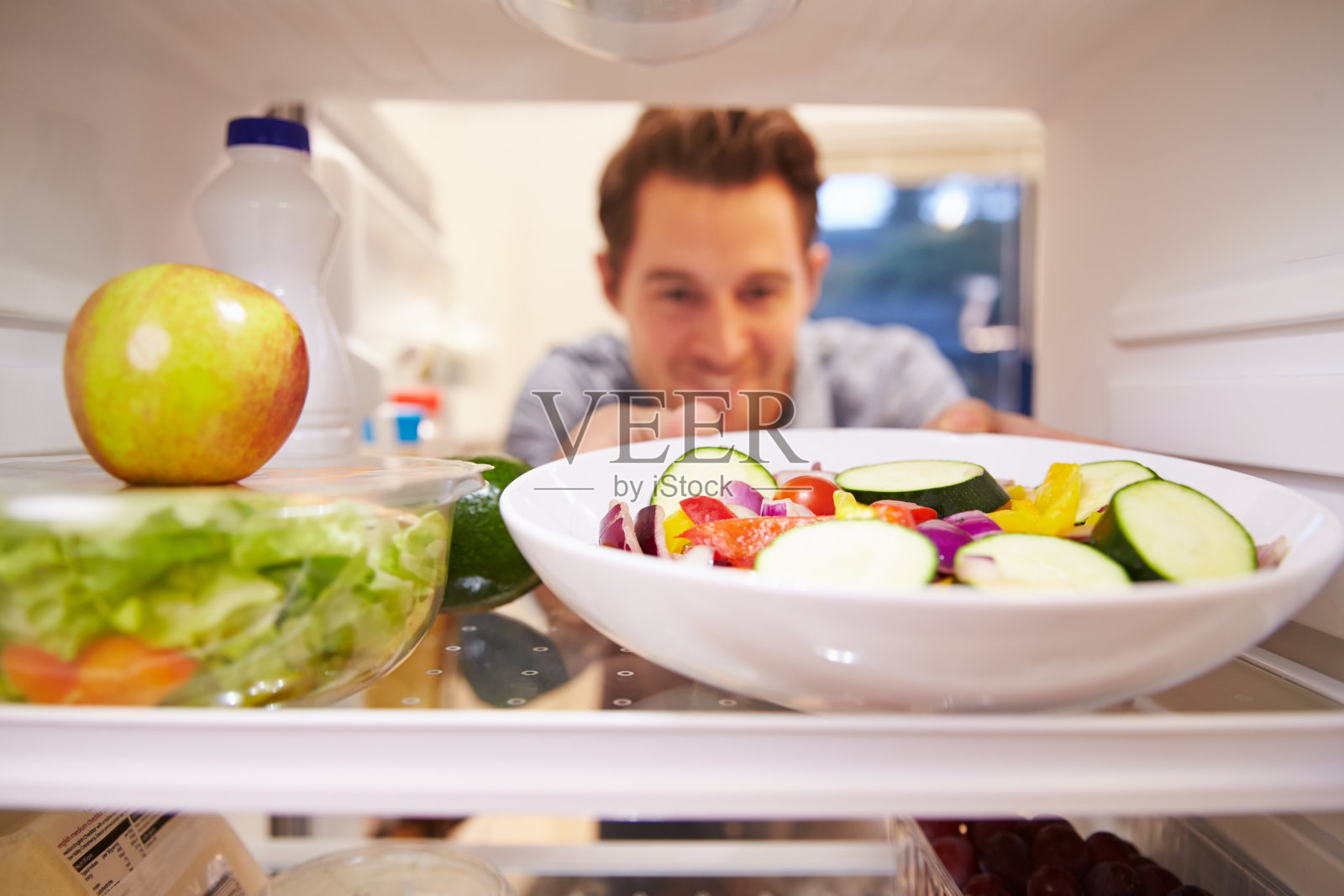 一名男子在看装满食物的冰箱并选择沙拉照片摄影图片