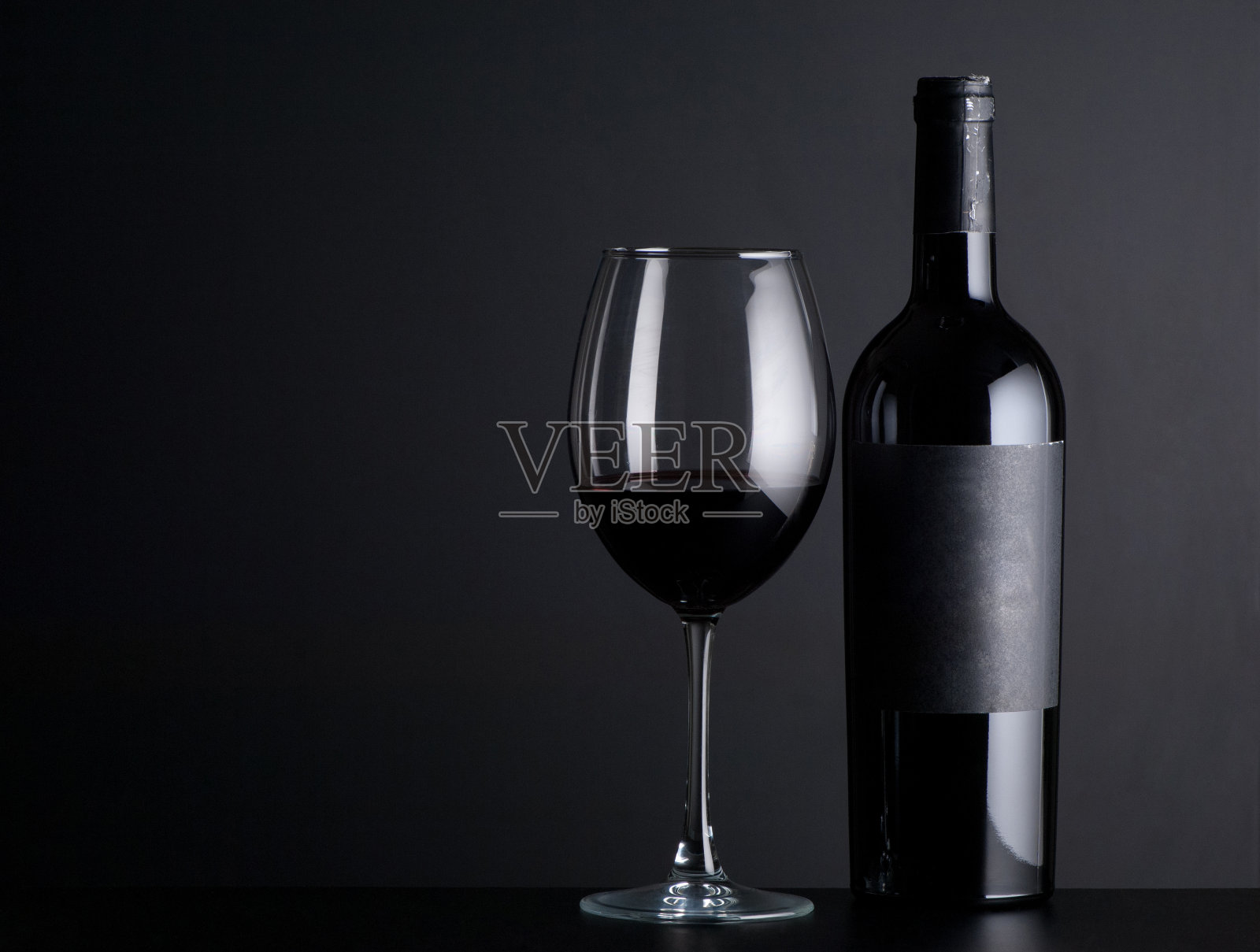黑色背景上的一瓶葡萄酒和一个玻璃杯照片摄影图片