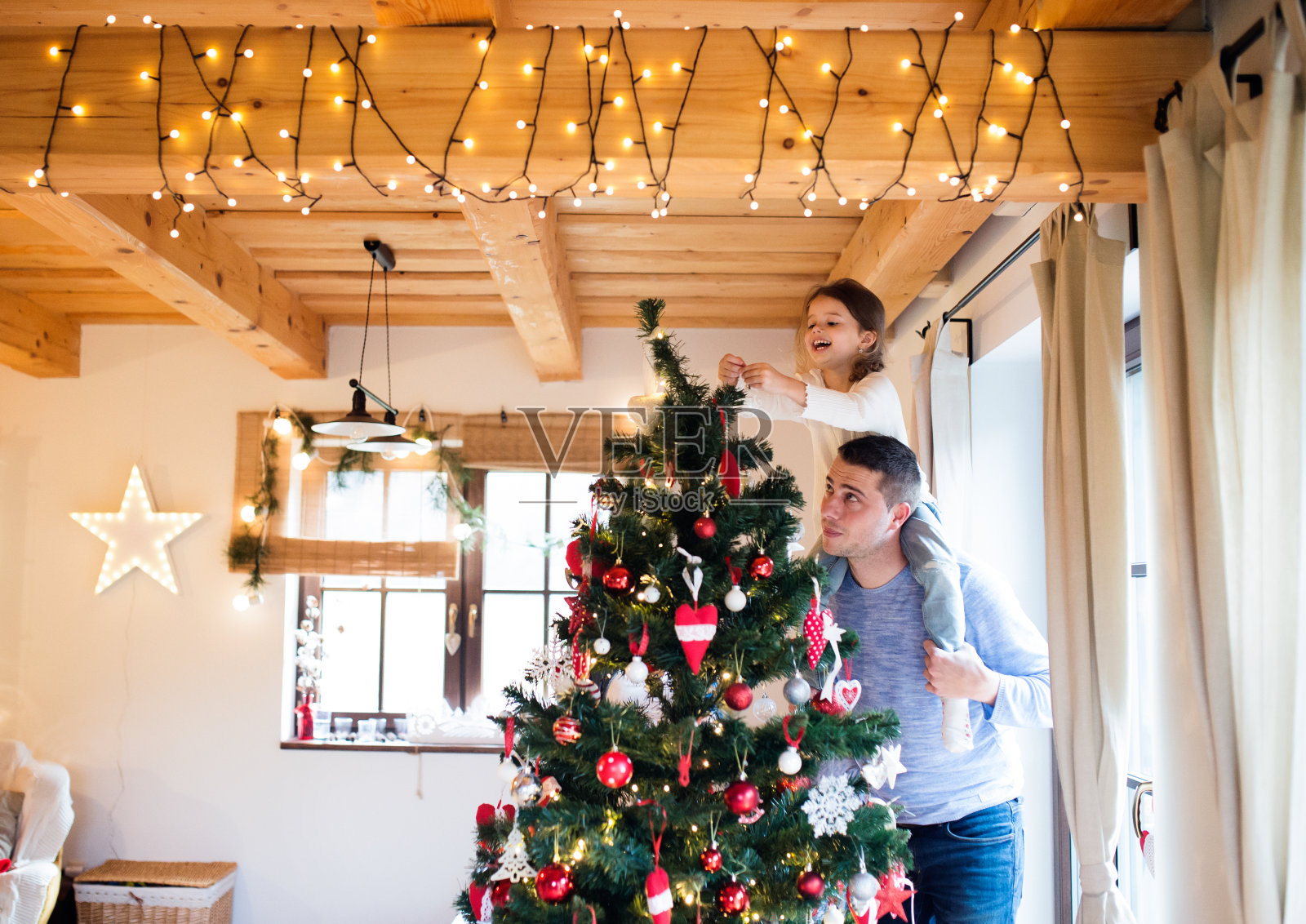 年轻的爸爸和女儿一起装饰圣诞树。照片摄影图片