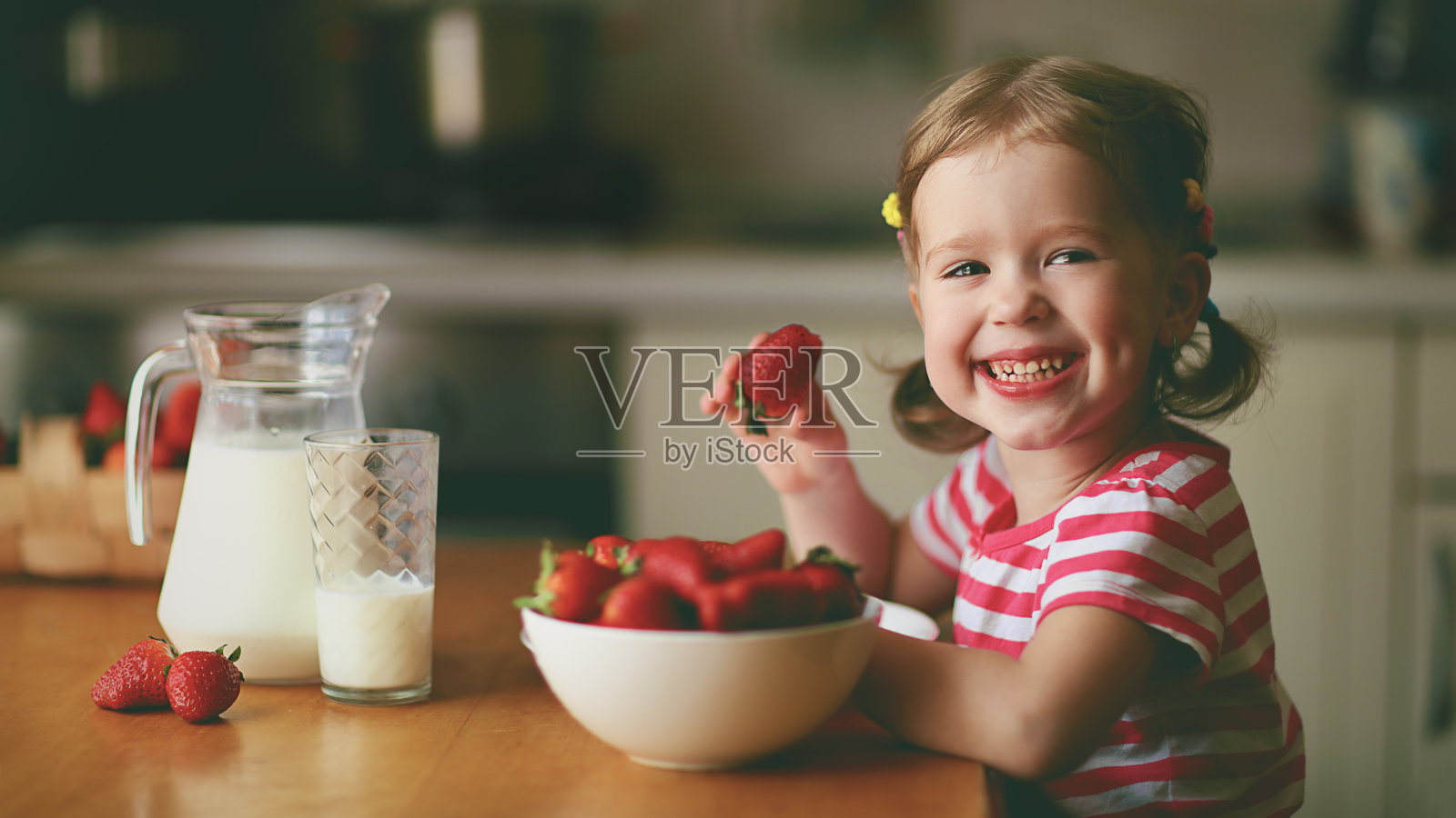 快乐的小女孩在夏天的家庭厨房里吃草莓照片摄影图片