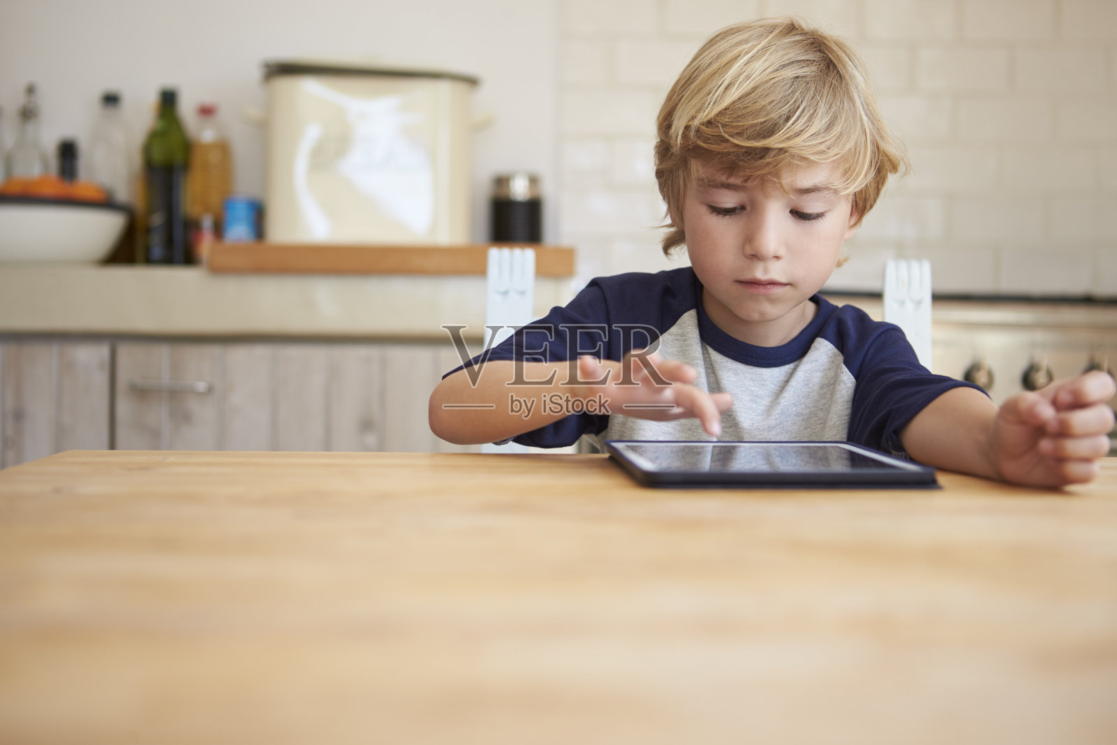 小男孩在餐桌上使用平板电脑，正面照片摄影图片