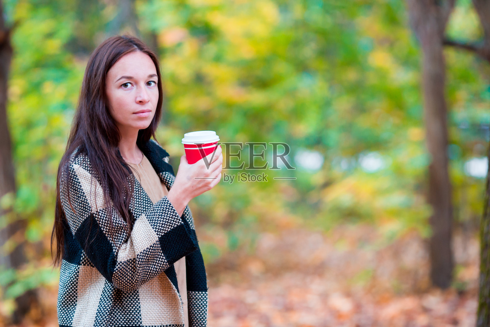 美丽的女人在秋天的树叶下喝咖啡秋天公园。照片摄影图片